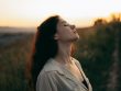 Woman standing with eyes closed in a field during sunset, exuding tranquility and peace.