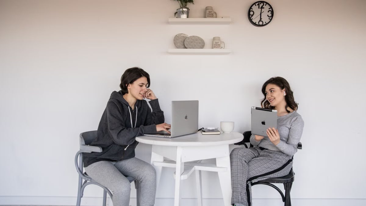 Casual remote work meeting with two women using laptops and tablets at home.